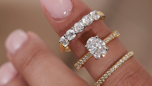 Close-up of an oval-cut diamond engagement ring with pav&eacute; band, styled with gold diamond eternity bands.
